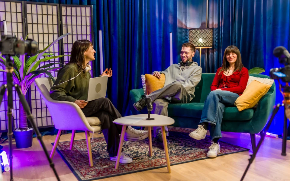 Três pessoas durante a gravação de uma entrevista em estúdio, com câmaras e microfones.