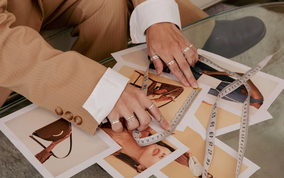 Mãos a organizar fotografias de moda e materiais de referência sobre uma mesa.